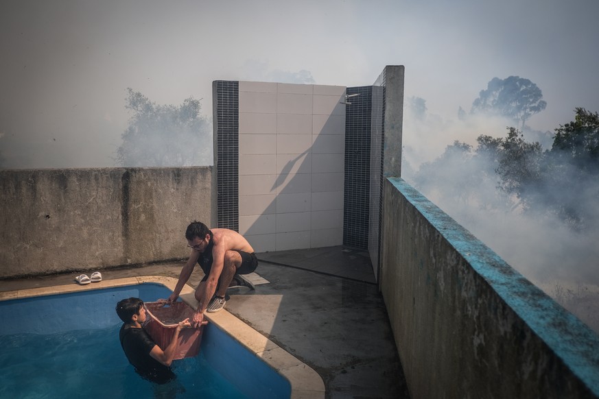 epa10064432 Locals fetch water from a swiming pool to pour onto the flames during a fire in Canecas, outskirts of Lisbon, Portugal, 10 July 2022. Portugal&#039;s President warned that the risk of fire ...