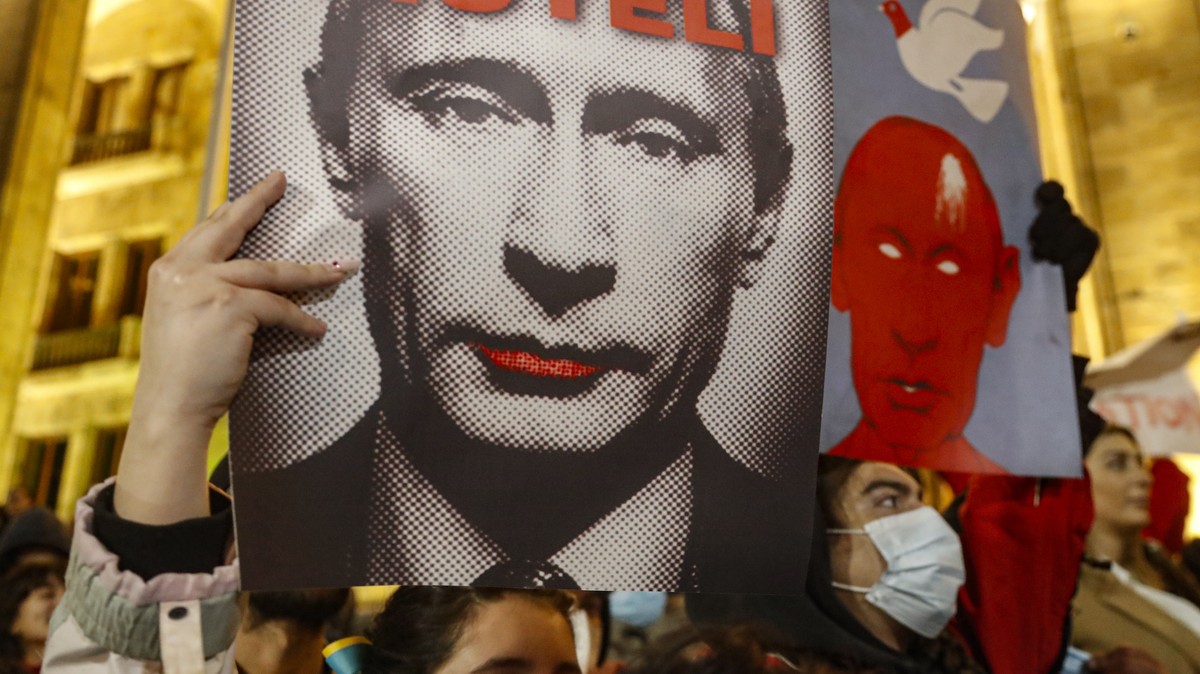 epa10511928 Supporters of Georgian opposition parties hold the posters with pictures of the Russian President Vladimir Putin attending an opposition rally n front of the Parliament building in Tbilisi ...