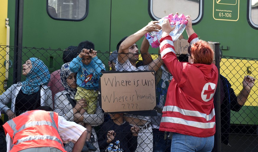 Helfer des Roten Kreuzes geben Flüchtlingen Wasser.<br data-editable="remove">