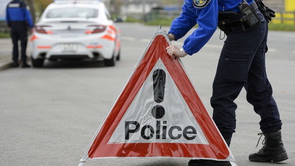 [Editor&#039;s note: photo mise-en-scene] A police officer from the cantonal police of Vaud installs a police warning triangle, in the foreground, while another officer stands next to a police car, in ...