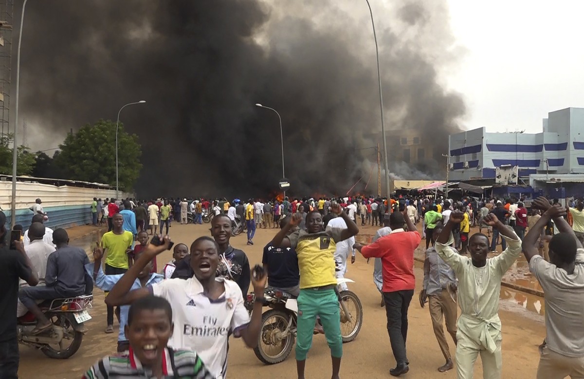 With the headquarters of the ruling party burning in the back, supporters of mutinous soldiers demonstrate in Niamey, Niger, Thursday, July 27 2023. Governing bodies in Africa condemned what they char ...