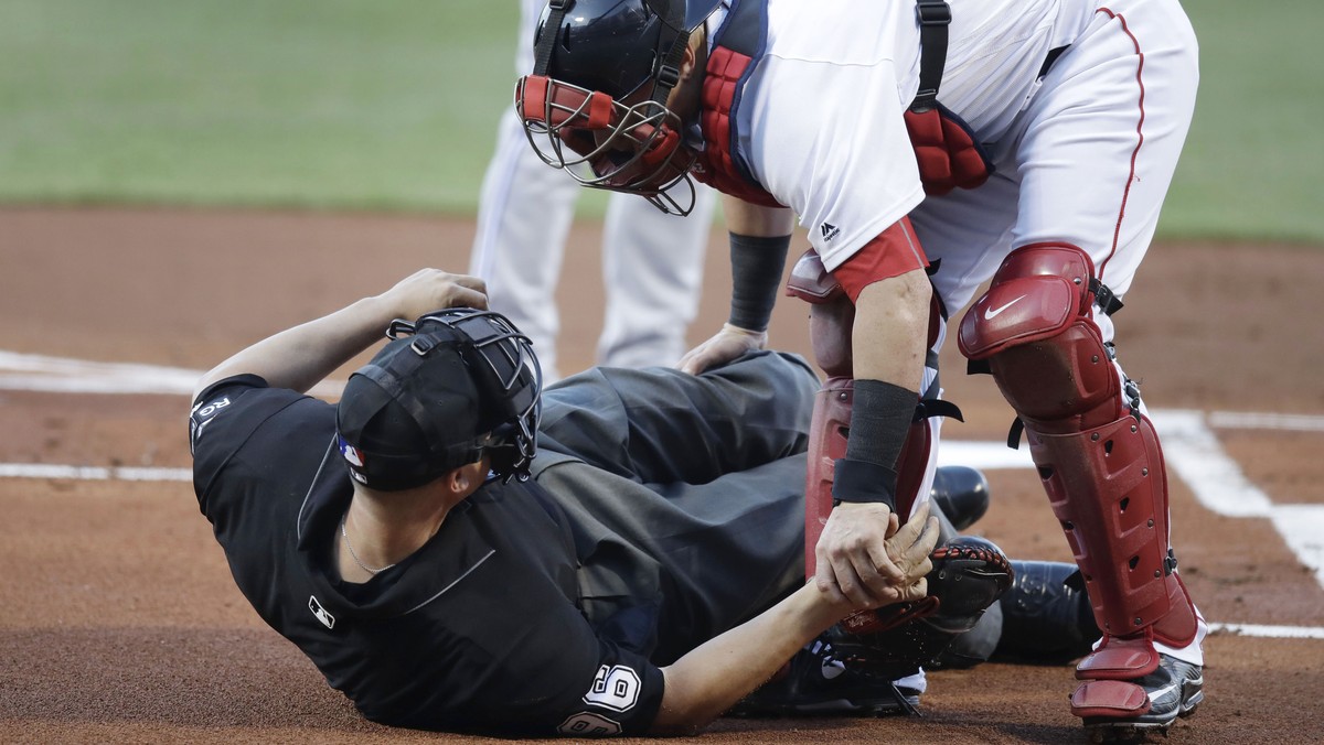 Boston Red Sox catcher Christian Vazquez aids home plate umpire Chris Segal after he was accidentally hit on the head by Toronto Blue Jays' Josh Donaldson's bat during the first inning of a  ...