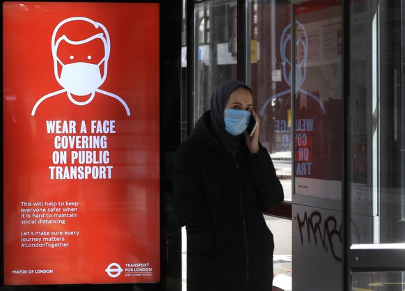 A passenger waits at a bus stop with a sign advising travellers to wear a face covering whilst travelling, in London, Friday, June 5, 2020. It will become compulsory to wear face coverings whilst usin ...