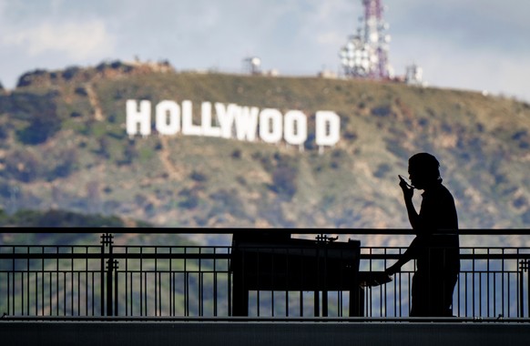 FILE - A worker wheels equipment past the famous Hollywood sign as preparations continue on March 8, 2023, for the 95th Academy Awards at the Dolby Theatre in Los Angeles. Television and movie writers ...