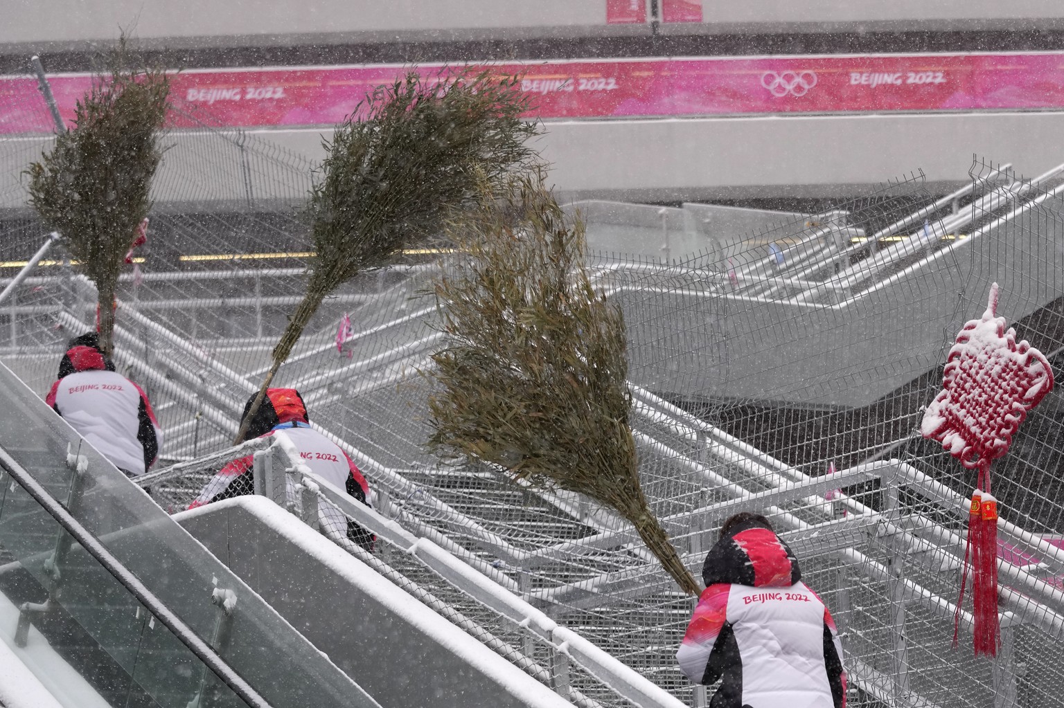 Workers use bamboo branches to clear the snow near the finish area of the alpine ski venue at the 2022 Winter Olympics, Sunday, Feb. 13, 2022, in the Yanqing district of Beijing. (AP Photo/Luca Bruno)