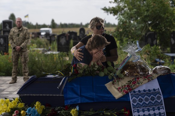 Comforted by Khrystyna Liubymska, top, Zynaida Nedoleshko weeps next to a casket carrying the remains of her nephew, Roman Shadlovskyi, during a reburial service for him in Bucha, Ukraine, Tuesday, Ju ...