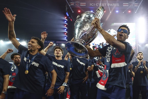 Paris Saint-Germain's French midfielder Desire Doue, right, holding the trophy, and captain Marquinhos, celebrate with teammates during a ceremony to present the trophy a day after Paris Saint-Ge ...