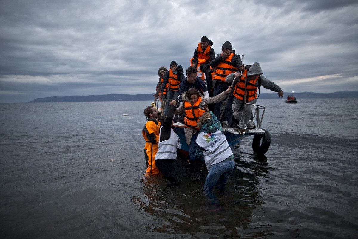 In this Thursday, Dec. 3, 2015 photo, volunteers help refugees disembark from a vessel carrying Yazidi refugee Samir Qasu, 45, from Sinjar, Iraq, and his wife Bessi, 42, their two daughters Delphine,  ...