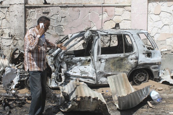 epa04512861 A man walks in front of a destroyed car at the scene where a suicide bomber attacked a United Nations convoy near the airport in Mogadishu, Somalia, 03 December 2014. Several people were f ...