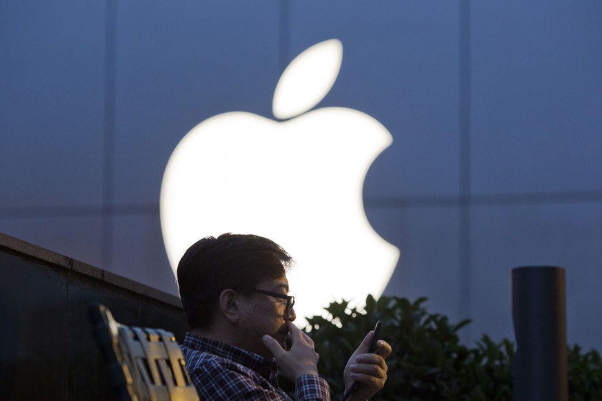 FILE - In this May 13, 2016 file photo, a man uses his mobile phone near an Apple store logo in Beijing, China. Apple Inc. has filed suit in China challenging Qualcomm Inc.’s fees for technology used  ...