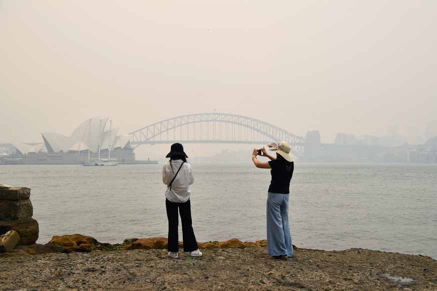 epa08058689 Tourists take photos on the rocks at Mrs. Macquarie&#039;s Chair as smoke and haze from bushfires in New South Wales blankets the CBD in Sydney, Australia, 10 December 2019. The New South  ...