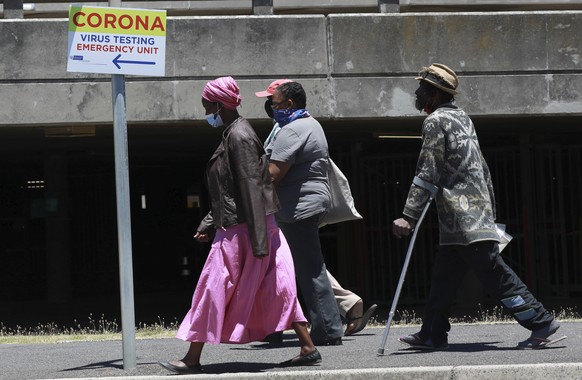 People pass a sign at Groote Schuur Hospital in Cape Town, South Africa, indicating a COVID testing station Tuesday, Dec. 29, 2020. South African President Cyril Ramaphosa has declared the wearing of masks compulsory and has reimposed a ban on the sales of alcohol and ordered the closure of all bars and beaches as part of new restrictions to help the country battle a resurgence of the coronavirus, including a new variant. (AP Photo/Nardus Engelbrecht)