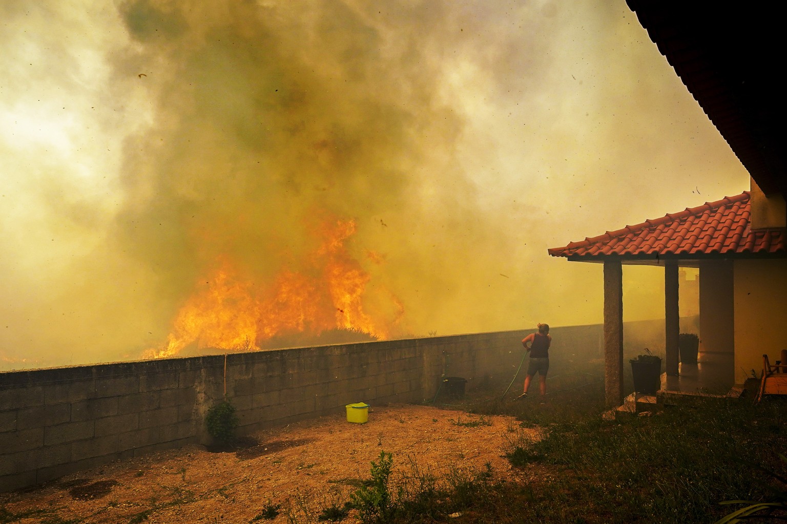 epa10072749 A local woman looks at the flames burning trees surrounding her house in Ancede village during a wildfire in the municipality of Baiao, North of Portugal, 15 July 2022. EPA/HUGO DELGADO