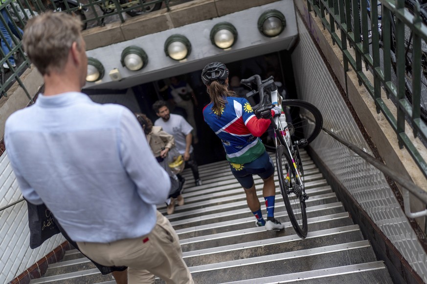 Vera Looser, of Namibia, carries her bike down into a metro station while surveying the course through Paris streets during a training session ahead of her road race event at the 2024 Summer Olympics, ...