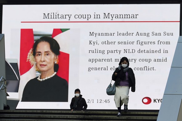 People wearing masks against the spread of the coronavirus walk in front of a screen showing the news on Myanmar situation Monday, Feb. 1, 2021, in Tokyo. Myanmar military television said Monday that  ...