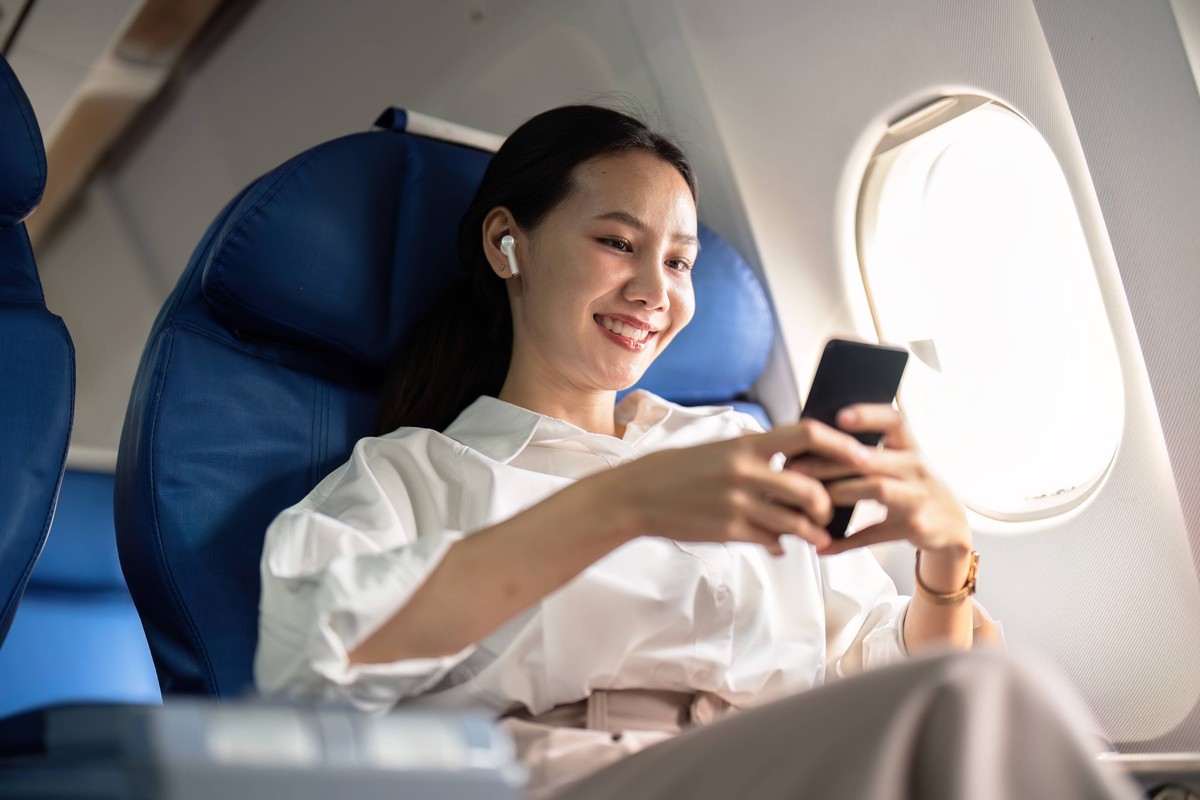 Traveling and technology. Flying at first class. Young business woman passenger using smartphone while sitting in airplane flight Traveling and technology. Flying at first class. Young business woman  ...