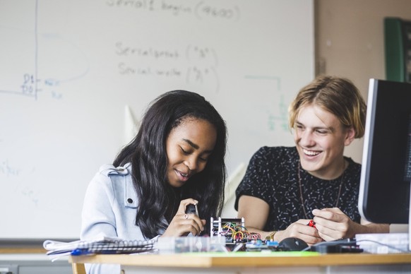Smiling female student preparing science project with young male friend on desk in classroom at high school , model released, property released Copyright: xMaskotx , MA65560