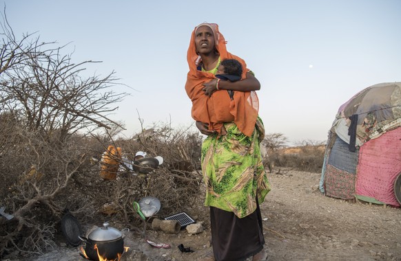 Fathiya Muhamed Hassen, one of among 200 households who arrived three months ago from north of Hargeisa looking for water and pasture following the drought, holds her child as she cooks in the village ...