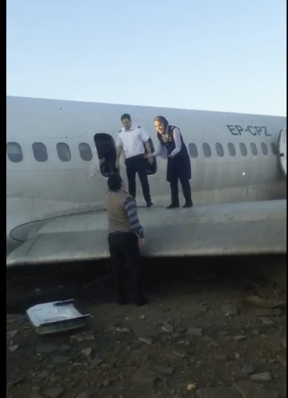 In this image from video shot by Iran's Civil Aviation Network News, a flight attendant speaks to an onlooker as passengers walk off over the wing of a crashed plane in Mahshahr, Iran, Monday, Ja ...