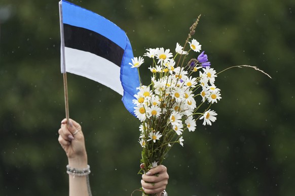 A woman waves Estonian flag and bouquet of flowers during the song festival, part of the "Iseoma" Song and Dance Celebration, at the Song Festival Grounds in Tallinn, Estonia, Sunday, July 6 ...