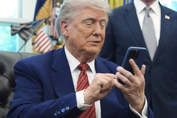 President Donald Trump silences his mobile phone which rang two times as he was speaking to reporters after signing executive orders regarding nuclear energy in the Oval Office of the White House, Fri ...