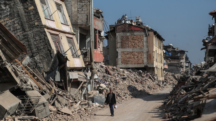 epa10485023 A man walks past collapsed buildings in the aftermath of powerful earthquakes in Hatay, Turkey, 23 February 2023. More than 46,000 people died and thousands more were injured after major e ...