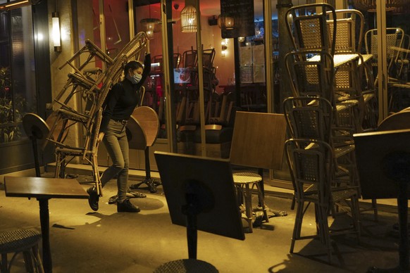 A woman carries chairs to close a bar terrace in Paris, Monday Sept. 28, 2020. French President Emmanuel Macron justified on Monday new restrictions in the country to limit the spread of the virus as  ...