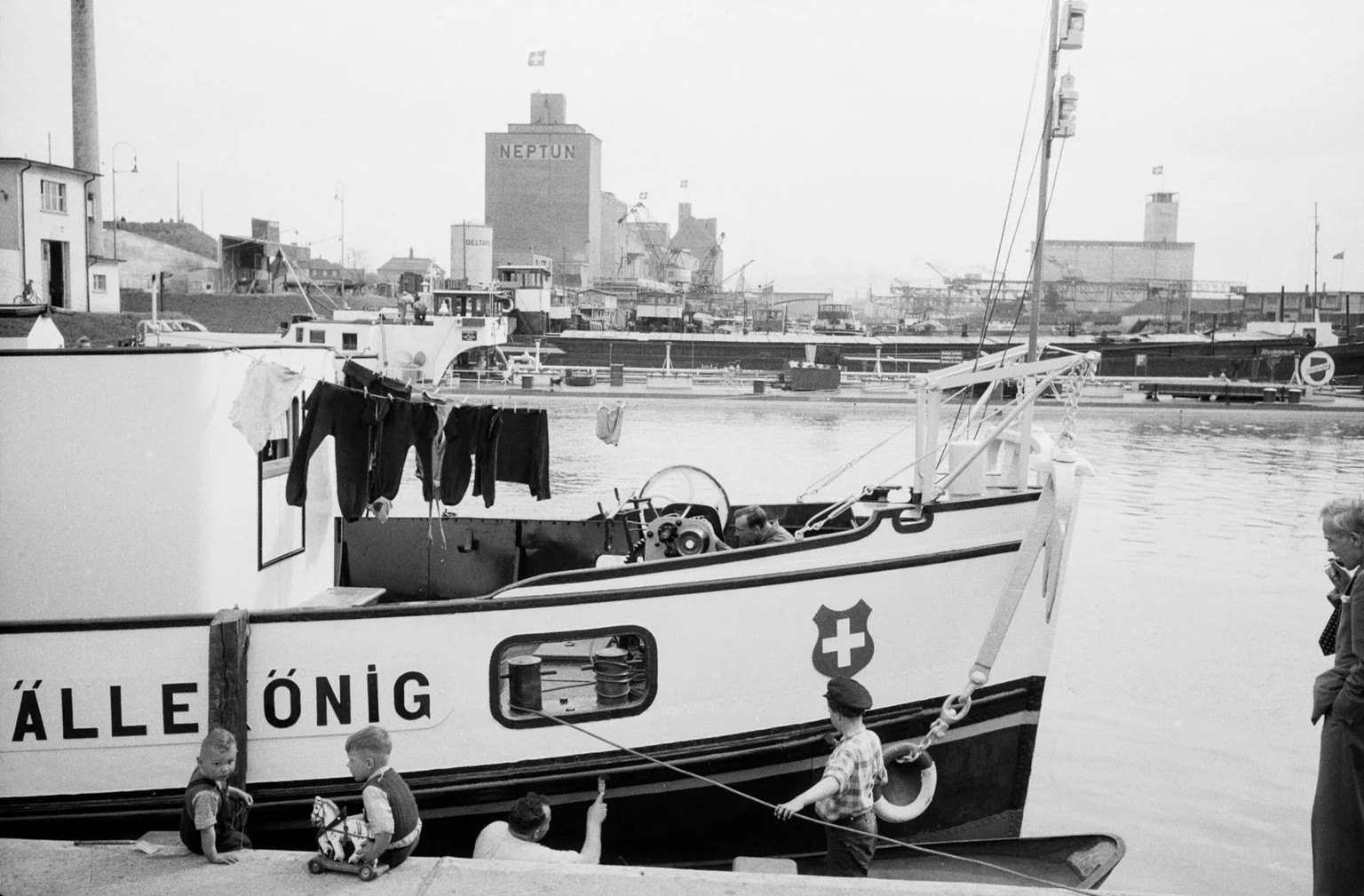 Kinder spielen vor dem Motorschiff «Lällekönig» im Hafen Basel-Kleinhüningen, 1955.
https://ba.e-pics.ethz.ch/#main-search-text=Rheinh%C3%A4fen&amp;main-search-mode=and&amp;detail-asset=3e1024e9-5891- ...