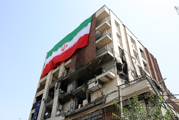 epa12196225 A large-scale national flag hangs from a damaged building that was hit by a recent Israeli airstrike, in Tehran, Iran, 25 June 2025, during a US-mediated ceasefire between Iran and Israel. ...