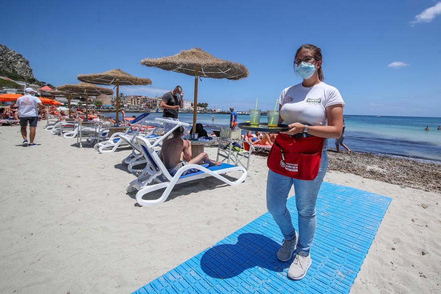 epa08469007 A waitress wearing face mask works as bathers take advantage of the first day after authorities ease the coronavirus lockdown to allow for sunbathe and to swim on the waterfront in the Mon ...