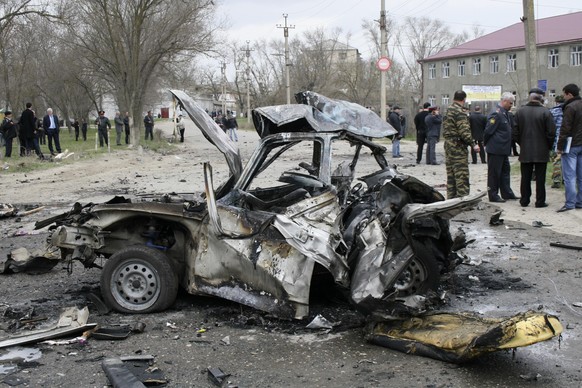 Investigators stand next to a damaged car at a site of an explosion in Kizlyar, a town in southern Russian region of Dagestan, Wednesday, March 31, 2010. Two suicide bombers including one impersonatin ...
