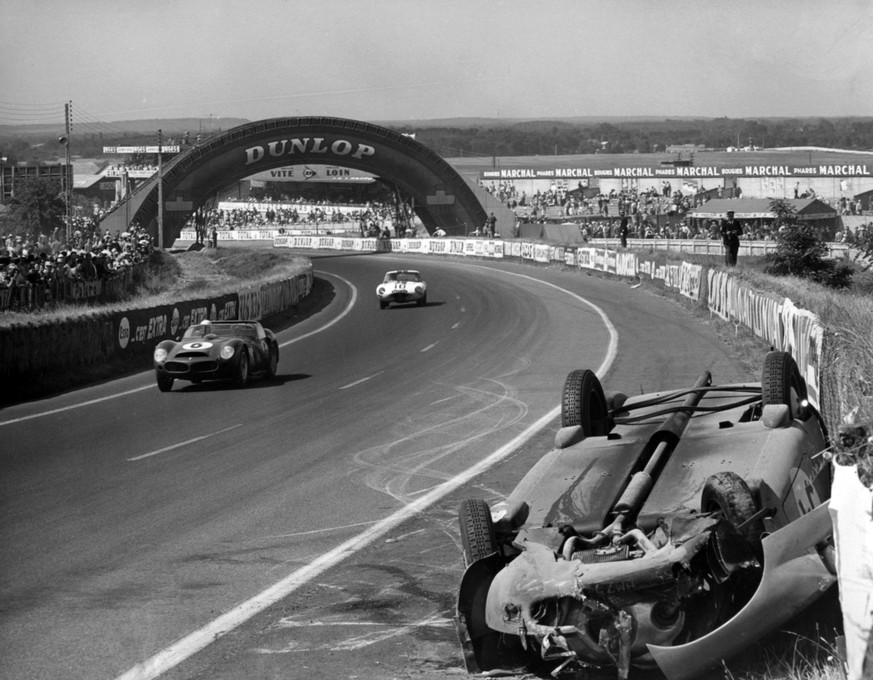 The winning 12 cyclinder Ferrari of Phil Hill of the United States and Olivier Gendebien of Belgium passes the overturned Panhard of Pierre Lelong and Jean Pierre Henriaud during the gruelling 24 hour ...