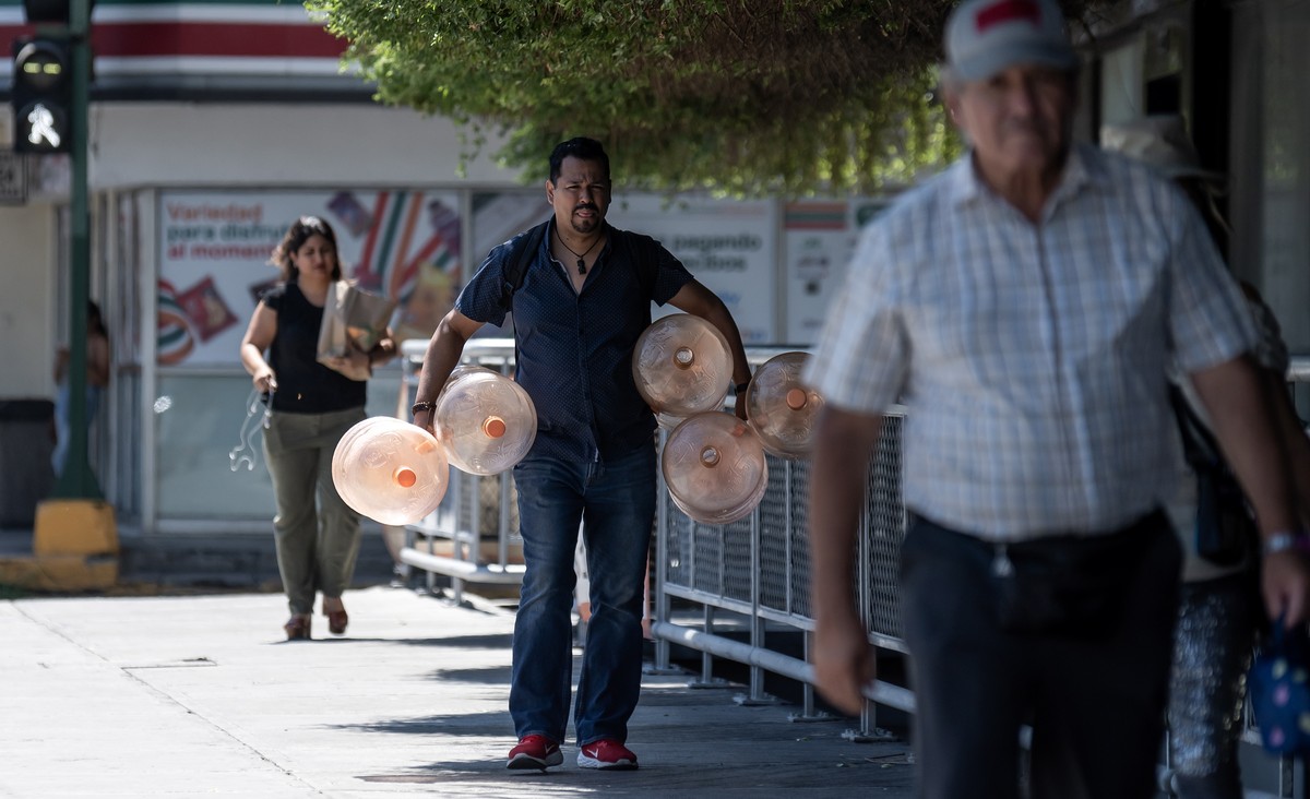 epa10716126 A man walks with jugs of water to be filled due to the high temperatures, in Monterrey, Nuevo Leon state, Mexico, 28 June 2023. The heat wave that hit Mexico has caused 36 deaths in the no ...