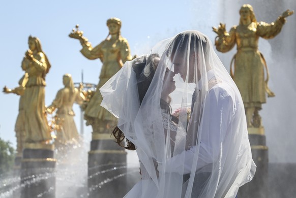 epa12229454 A bridal couple cool off near the Druzhba Narodov (Friendship of Nations) Fountain on a warm day at the All-Russian Exhibition Center in Moscow, Russia, 10 July 2025. The Moscow region is  ...