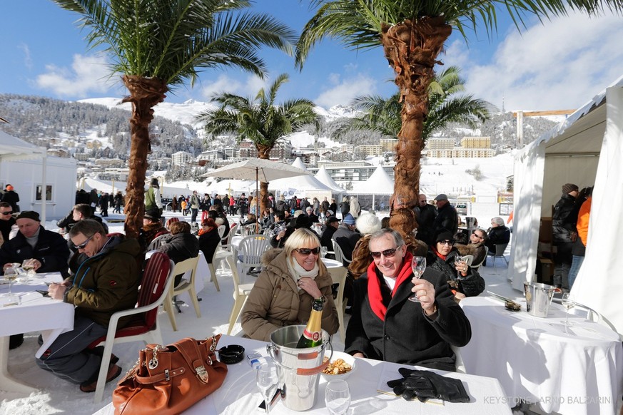 Gaeste geniessen unter Palmen das sonnige und milde Wetter vor einem Restaurant auf dem gefrorenen St. Moritzersee in St. Moritz am Sonntag, 9. Februar 2014. (KEYSTONE/Arno Balzarini)