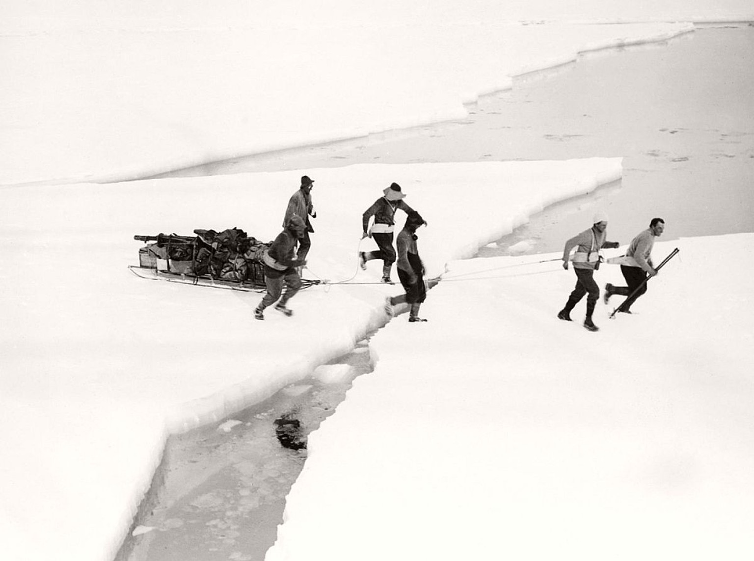 Derweil schleppen die Mitglieder der geologischen West-Abteilung einen Schlitten über das Meereis. Das Team unter der Leitung des Geologen T. Griffith Taylor war das erste, das die westlichen Berge de ...