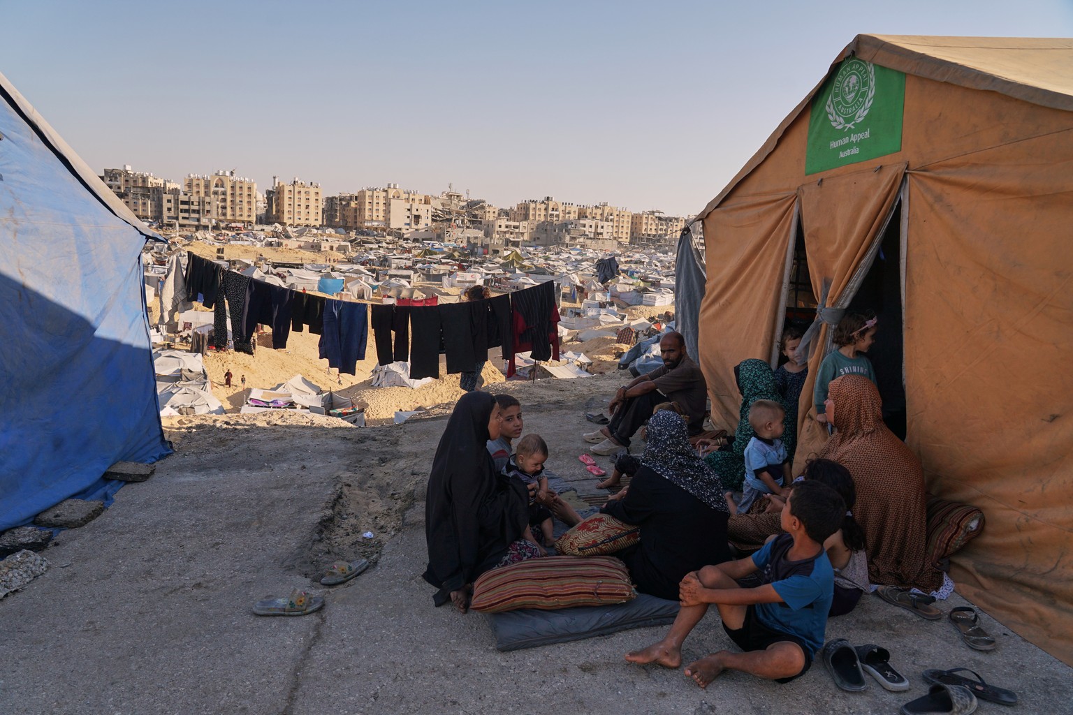 Members of Al-Kafarna family, who were evacuated from Gaza City, sit in front of their tent in a camp for displaced Palestinians in Muwasi, an area that Israel has designated as a safe zone, in Khan Y ...
