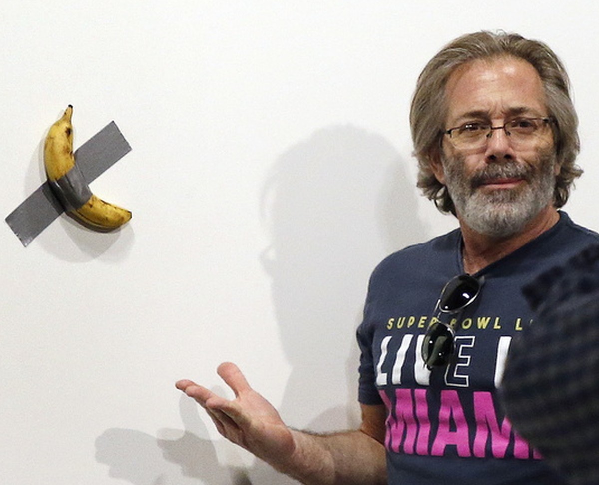 epa08047505 Art patrons take a picture with Italian artist Maurizio Cattelan piece's 'Comedian' (a banana duct taped to the wall) during Art Basel in Miami, Florida, USA, 05 December 20 ...