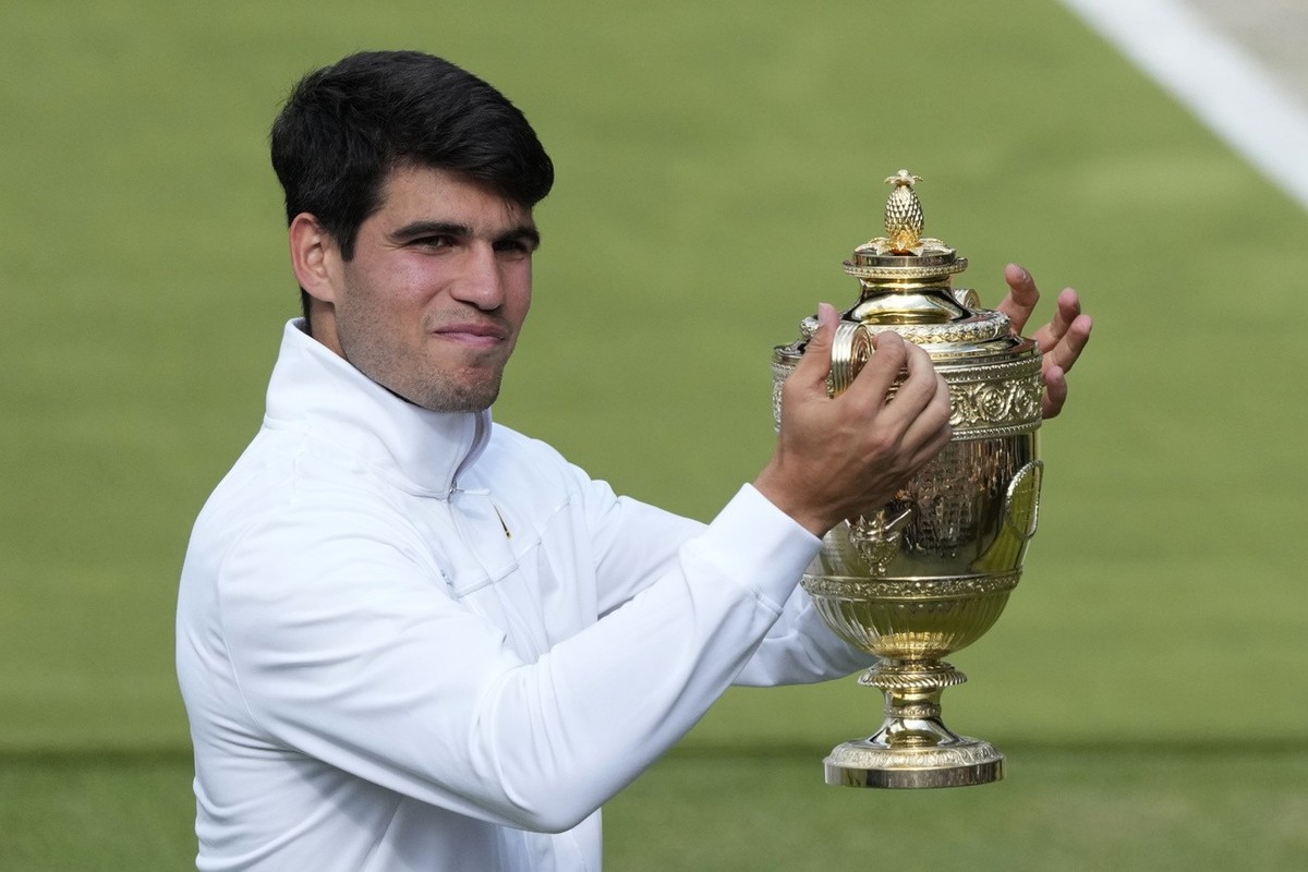 Carlos Alcaraz of Spain smiles as he holds up his trophy for the photographers after defeating Novak Djokovic of Serbia in the men's singles final at the Wimbledon tennis championships in London, ...
