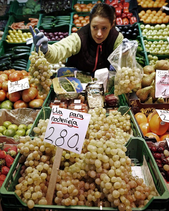 epa04542138 A woman holds a white grape bunch in her fruits and vegetables stall at a market in Pamplona, Spain, 29 December 2014. Each year, Spaniards greet the New Year eating 12 white grapes to the ...