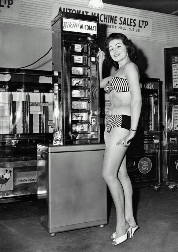 Woman in bikini standing by bikini vending machine, portrait (B&amp;W)
