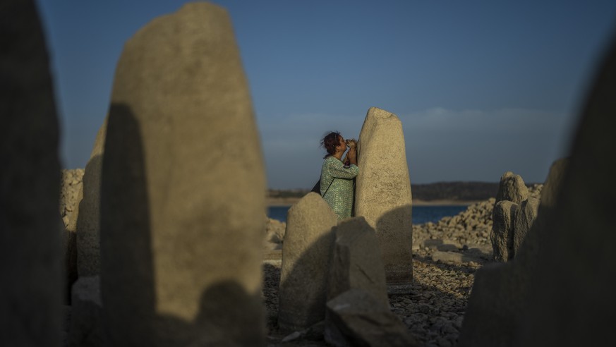Amalie Garcia, 54, stands with her dog next to The Dolmen of Guadalperal, a megalithic monument that emerged due to drought at the Valdecanas reservoir in El Gordo, western Spain, Saturday, Aug. 13, 2 ...