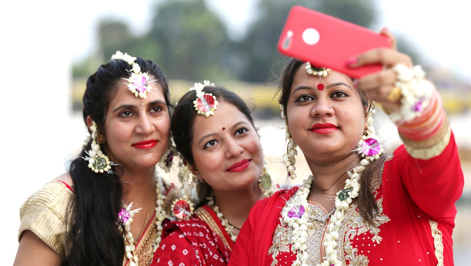 epa06091130 Newly married Indian women, wearing ornaments made of flowers as a tradition, take selfies with their cell phone as they visit to pay obeisance at the Laxmi Narayan temple during the ongoi ...