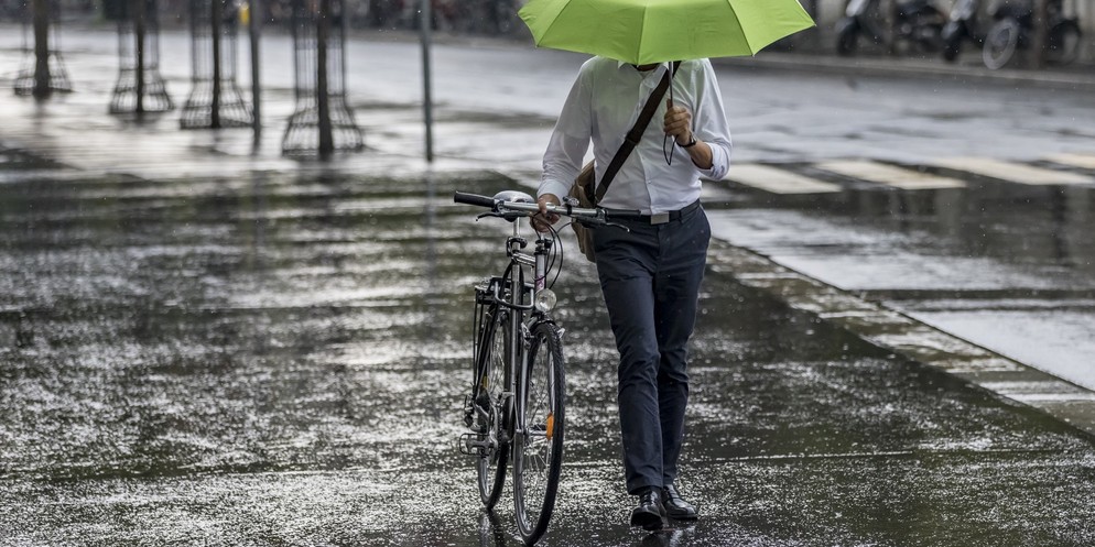 Ein Mann mit einem Schirm ist in Bern mit seinem Velo im Regen unterwegs.
