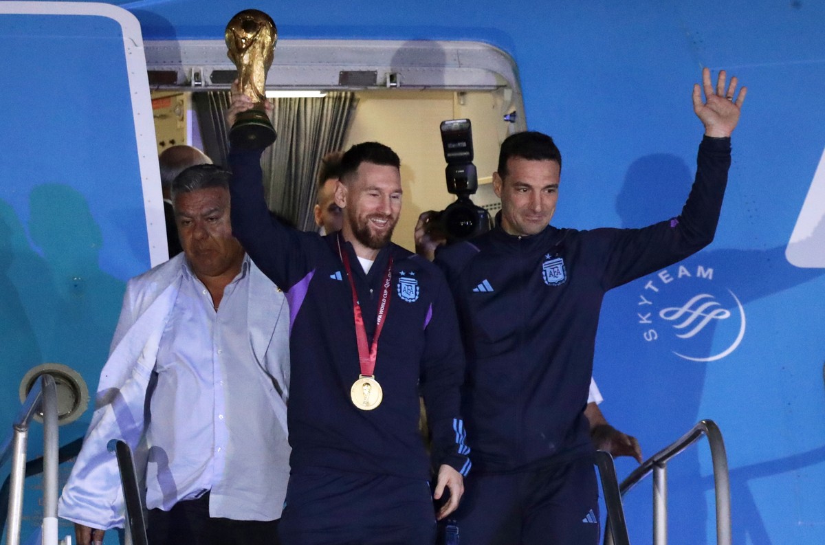 epa10374424 Lionel Messi (C) of the Argentina national soccer team descends a plane with the trophy of Qatar 2022 World Cup accompanied by head coach Lionel Scaloni (R), upon ther arrival to the Inter ...