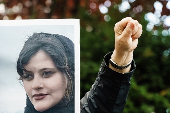 epaselect epa10195345 A protester of the National Council of Resistance of Iran (NWRI) gestures during a demonstration with her fist, while being covered by a placard, showing deceased Mahsa Amini, in ...