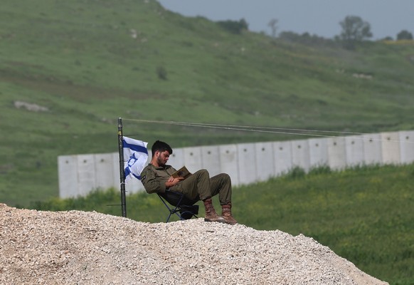 epa12897835 An Israeli soldier reads a book next to an Israeli flag, near the security barrier between Israel and Lebanon near Avivim, Northern Israel, 18 April 2026. Israel and Lebanon have agreed to ...