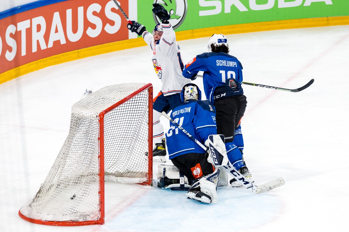 Justin Schuetz of EHC Red Bull Muenchen, center, scores his team's fifth goal of the game under pressure from Dominik Schlumpf, right, and goaltender Luca Hollenstein of EV Zug during the Champio ...