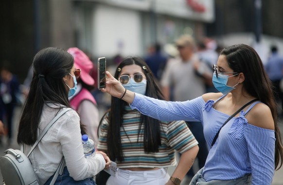 14.03.2020, Mexiko, Mexiko-Stadt: Junge Frauen mit Mundschutzmasken stehen zusammen auf einer Straße, eine der Frauen macht ein Selfie. Das neuartige Coronavirus hat sich inzwischen in fast allen Länd ...