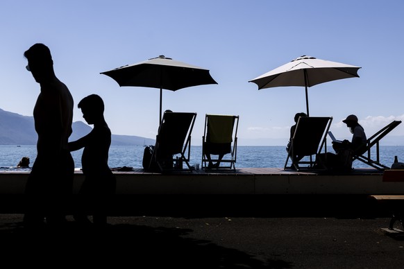 People take a break under an umbrella and enjoy the warm summer weather on the shores of Lake Geneva in front of the Swiss Alps mountains, in Vevey, Switzerland, Saturday, July 8, 2023 (KEYSTONE/Cyril ...